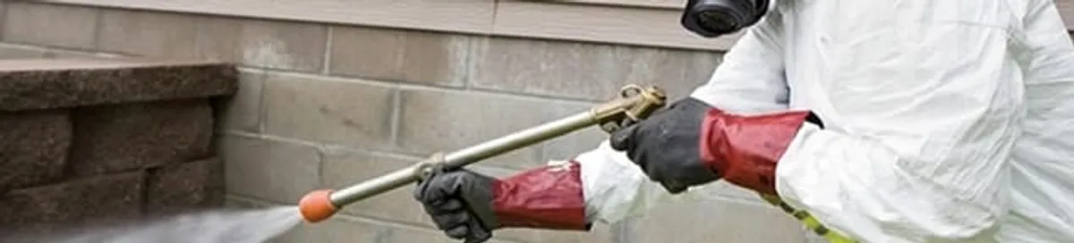 Pest control technician applying exterior insect treatment along a home foundation in Stamford, CT