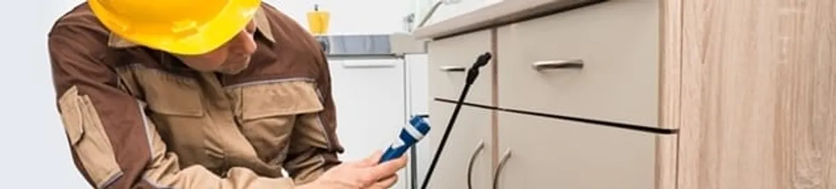 Roach exterminator applying treatment under kitchen cabinets in Stamford, CT