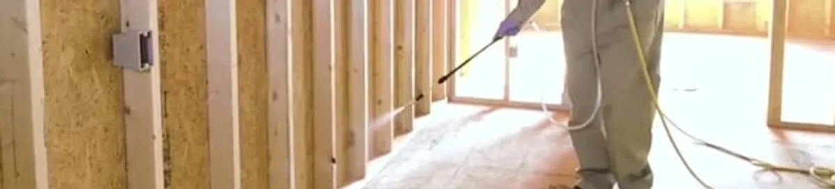 Termite treatment technician applying spray along framing and unfinished walls in Stamford, CT